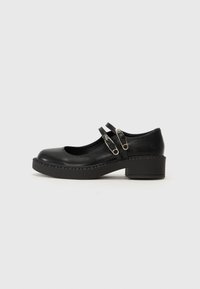 Black leather Mary Jane shoes with a rounded toe, two strap details, and a chunky heel. Features stitched edges and a smooth texture.