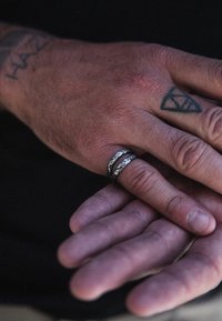 Srebrni i crni prstenovi na ruci, s teksturiranom površinom i prepoznatljivim slojevitim dizajnom. Vidljiva tetovirana koža.