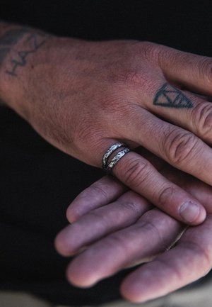 Sidabriniai ir juodi žiedai ant rankos, turintys tekstūruotą paviršių ir išskirtinį sluoksniuotą dizainą. Matoma tatuiruota oda.