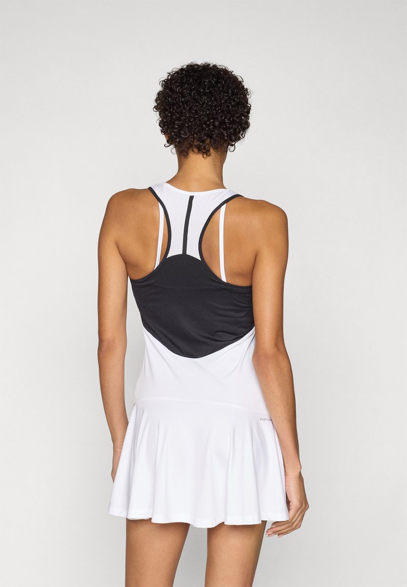 Robe de sport blanche avec un corsage en mesh noir ajusté, des bretelles en dos nageur et une jupe évasée. Texture lisse, design minimaliste.