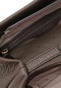 Interno di borsa in pelle marrone lavorata con una tasca con cerniera e una fodera liscia e decorata in tonalità marrone chiaro.