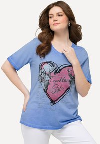 Camiseta de algodón azul con un gráfico de corazón que presenta ciervos, elementos florales y texto escrito a mano. Manga corta y escote en forma de barco.