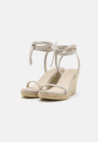 Beige kile sandals med en jute-bekledd hæl, minimalistiske krysstriper og ankelbånd, laget av et mykt og glatt materiale.