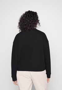 Sudadera negra con un corte relajado, puños y dobladillo de canalé. Textura suave con un diseño simple, sin logotipos ni patrones visibles.