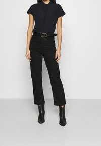 Blouse marine à manches courtes avec un détail de nœud au col, associée à un pantalon noir taille haute et des bottines noires à bout pointu.
