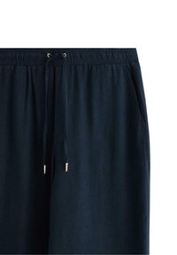 Pantaloni blu navy in linea morbida con cintura elastica, dettagli con cordoncino e tasche laterali. Realizzati in tessuto morbido e leggero.