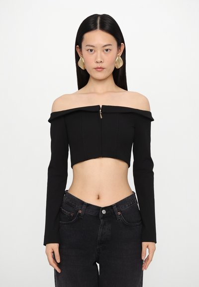 Černý crop top bez ramínek s dlouhými rukávy, který má přední zip a přiléhavý střih. Kombinováno s černými džíny s vysokým pasem.