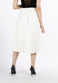 Witte plooienrok met een elastische tailleband, gecombineerd met stijlvolle zwarte hoge hakken. Achtergrond is effen wit.