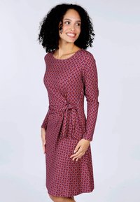 Figurbetontes Kleid aus leuchtendem lila Stoff mit einem mehrfarbigen Wirbelmuster. Lange Ärmel mit einem geknoteten Taillendetail, glatte Textur.