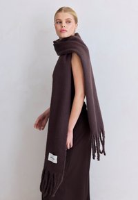 Écharpe en laine marron foncé avec bords frangés, drapée autour de l'épaule. Porte une étiquette avec "ARCHOX" sur le bord inférieur. Texture lisse.