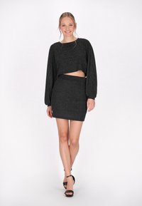 Svart, metallisk crop top med långa ärmar och en matchande minikjol. Slät textur; det figursydda design framhäver midjan. Höga svarta sandaler.