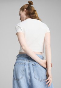 Bela skrajšana majica s kratkimi rokavi, teksturiran material; v kombinaciji z visokim pasom svetlo modra jeans krilo, ki ima štiri žepe.