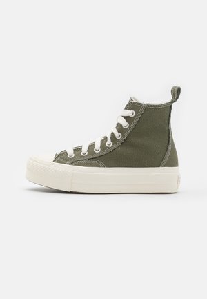 Baskets montantes en toile vert olive avec des lacets blancs et une semelle épaisse en caoutchouc blanc sur fond blanc uni.