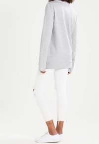 Felpa grigia con maniche lunghe, vestibilità rilassata. Abbinata a jeans skinny bianchi con ginocchia strappate e orli sfrangiati. Sneakers bianche.