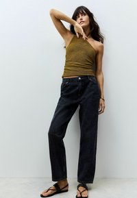 Brauner Strickoberteil mit asymmetrischem Ausschnitt, kombiniert mit hochtaillierten schwarzen Jeans. Schwarze Flip-Flops runden den Look ab.