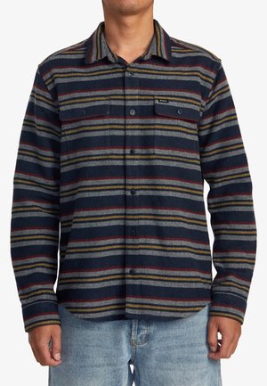 Mann trägt ein langärmeliges Hemd mit Knöpfen, horizontalen Streifen in Navy, Grau, Rot und Senfgelb sowie zwei mit Knöpfen verschließbare Brusttaschen.