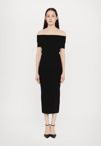 Black off-the-shoulder dress featuring a fitted silhouette, knee-length hem, and smooth, stretchy fabric. Paired with black pointed heels.