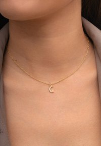 Collar de cadena de oro con un pequeño colgante de luna creciente adornado con pequeñas piedras transparentes en el cuello de una persona.