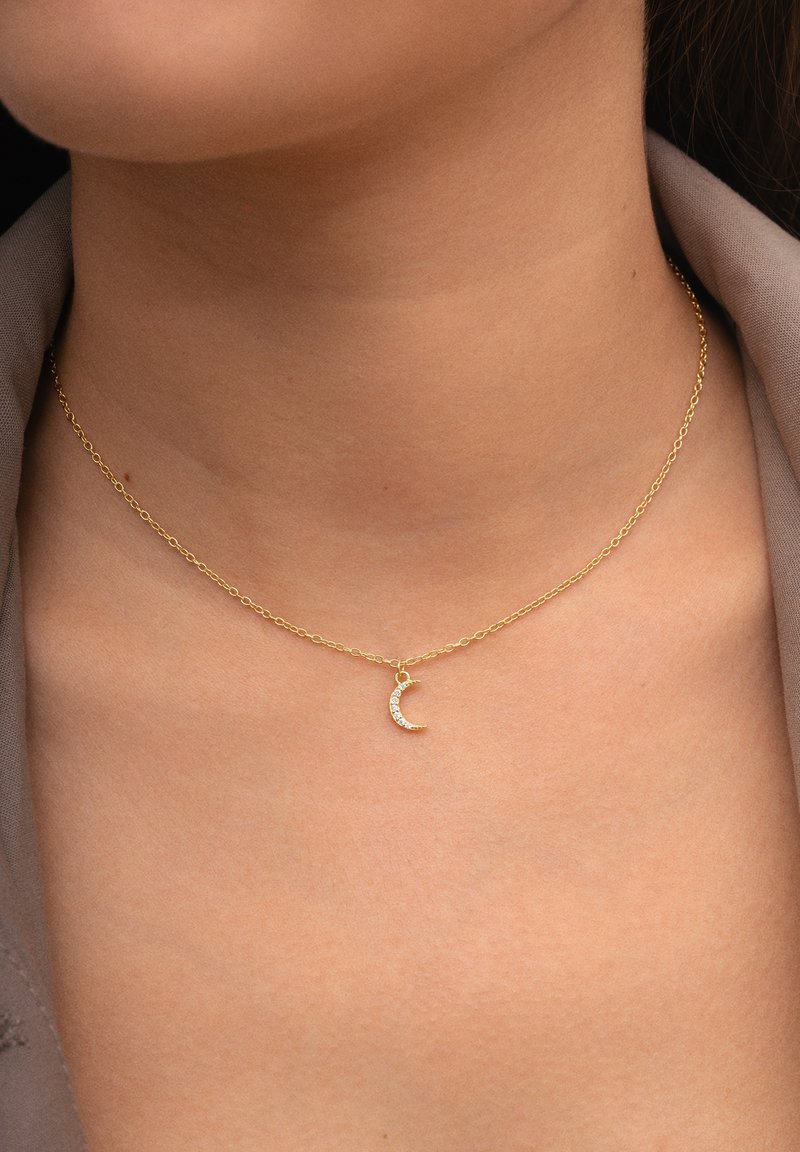 Collar de cadena de oro con un pequeño colgante de luna creciente adornado con pequeñas piedras transparentes en el cuello de una persona.