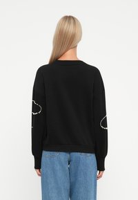 Sweatshirt noir à manches longues, avec des accents en perles au niveau des coudes. Fabriqué en tissu doux, avec une coupe décontractée et un ourlet côtelé.