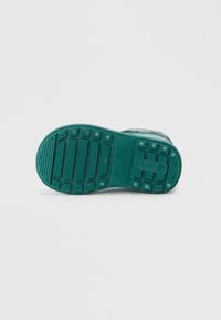 Semelle de chaussure en caoutchouc vert avec des nervures et motifs texturés. Comprend des marquages de taille et un logo. Conception de bout plat et arrondi.