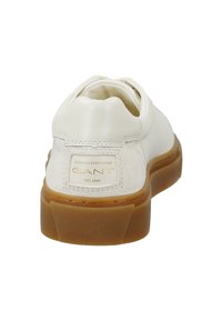 Bílé kožené tenisky se semišovými akcenty, kulatou špičkou a hnědou gumovou podrážkou. Obsahují zlatou logo nášivku na patě. Texturovaná podešev.