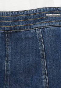 Traperice tamnoplave boje, s zlatnim šavovima, glatkim pojasom i metalnom oznakom na stražnjem dijelu.