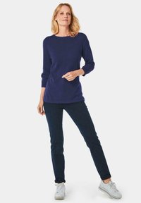 Marineblaues, langärmliges Oberteil aus weichem Stoff, kombiniert mit dunklen Jeans und weißen Sneakern. Schlichtes Design mit rundem Ausschnitt und figurbetonter Silhouette.