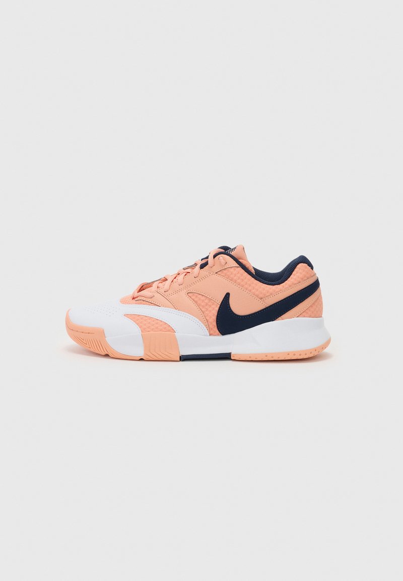 Nike atletiksko med en ferskenfarvet mesh-overdel, marineblå accenter, hvid mellemsål, struktureret design og en gummisål for godt greb.