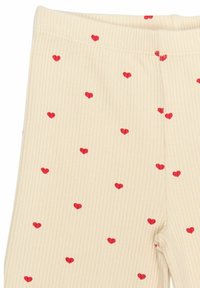 Kreemjad legginsid ribatatud tekstuuriga, kaunistatud väikeste punaste südamekestega hajusalt. Ülaservas elastne vöö.