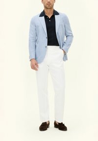 Blazer a scacchi azzurro chiaro su un polo blu navy, pantaloni bianchi e scarpe in suede marrone scuro. Il blazer ha revers a invitare e due tasche frontali.