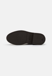 Dark rubber sole of a shoe with a textured surface, rounded shape, and a central groove. Minimal branding and simple design.