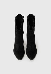 Bottines en daim noir avec des orteils pointus, ornées de motifs occidentaux en relief et de boucles de tirage sur les côtés. Texture lisse et design ajusté.