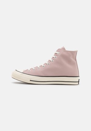 Baskets montantes en toile rose clair avec lacets blancs et semelle épaisse blanc cassé comportant des bandes noires.