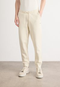 Crèmekleurige sweatpants van zacht materiaal, met een elastische tailleband met koord en zijzakken, tapered leg design.