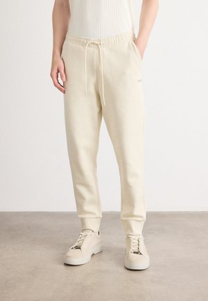 Cremefarbene Sweatpants aus weichem Stoff, mit elastischem Bund und Kordelzug, seitlichen Taschen und schmal zulaufendem Bein.