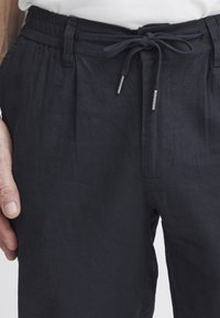 Navy woven trousers with an elastic waistband and drawstring. Features two front pockets, a relaxed fit, and textured fabric.