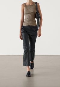 Femme marchant, portant un haut marron sans manches en maille, un pantalon court en cuir noir, des mocassins noirs, et portant un sac à épaule noir.