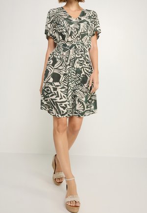 Kurzärmeliges Kleid in Grün und Creme mit Blattmuster, ausgestattet mit V-Ausschnitt und elastischem Taillenbund, kombiniert mit Keilsandalen.