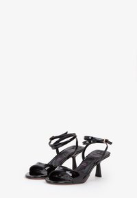 Sandali con tacco alto in vernice nera, aperti sulle dita, con cinturini alla caviglia e tacco a blocco. Presentano una texture liscia e un design minimalista.