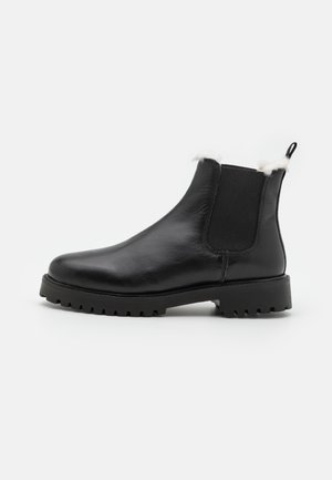 Bottes cheville en cuir noir avec panneaux latéraux élastiques, semelle en caoutchouc texturée et bordure en fourrure blanche en haut. Design élégant à bout rond.