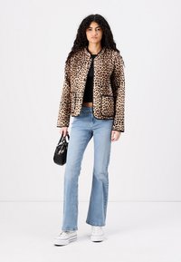Leopard print jacket with rounded neckline, patch pockets, and black trim, paired with light blue flared jeans and white platform sneakers.