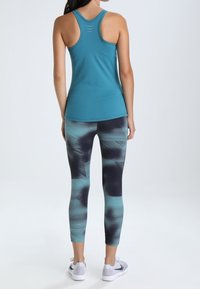 Turkusowy sportowy top na ramiączkach i czarne legginsy capri z turkusowym i ciemnym wzorem, zestawione z białymi butami do biegania.