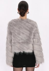 Grijze nepbont cropped jacket met lange mouwen, textuur van bont en een rechte zoom, gecombineerd met een zwarte mini rok.
