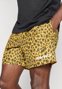 Calções amarelos com um padrão preto de leopardos. Feitos de material leve, com um detalhe de logo branco na bainha.