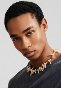Kralenketting gemaakt van onregelmatige, gebroken witte stukken, gedragen over een ribbeltrui in donkergrijs. Glad van structuur met variërende vormen.