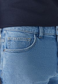 Jeans in denim azzurro chiaro con una texture liscia, caratterizzati da un design classico con cinque tasche e dettagli cuciti lungo le cuciture.