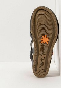 Sandale noire avec une semelle en caoutchouc brun texturé, présentant un logo orange et un design simple avec des sangles réglables et un bout ouvert.