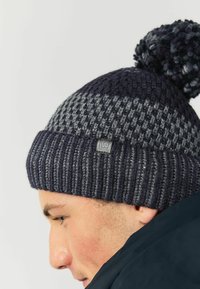 Knit beanie in navy and gray hues, featuring a textured pattern, ribbed cuff, and a pom-pom on top. Includes a small logo tag.