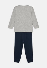 Siva majica dugih rukava uparena s hlačama od elastina tamnoplave boje, položena ravno na bijeloj podlozi, prikazuje stražnju stranu odjevne kombinacije.